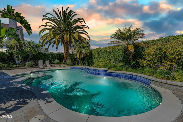 pool at dusk featuring a pool with connected hot tub and a fenced backyard