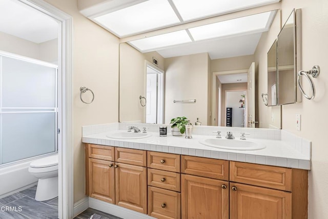 bathroom with toilet, double vanity, and combined bath / shower with glass door