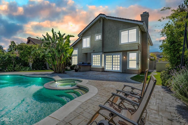 pool at dusk featuring a patio area, french doors, and a pool with connected hot tub