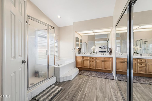 full bathroom featuring a stall shower, a bath, double vanity, vaulted ceiling, and healthy amount of natural light