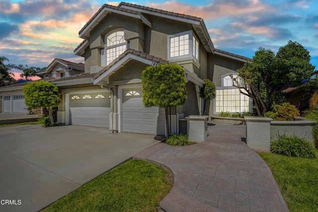 traditional home with stucco siding, a garage, driveway, and a tiled roof