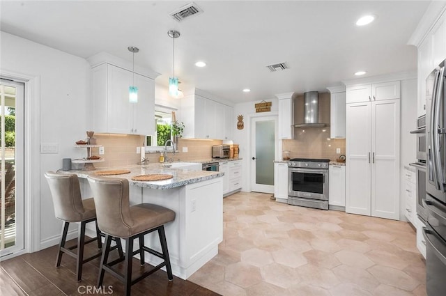 kitchen featuring stainless steel appliances, wall chimney exhaust hood, a peninsula, healthy amount of natural light, and recessed lighting
