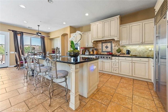 7940 Choi Dr, Riverside, CA 92506 - kitchen featuring cream cabinets, tasteful backsplash, an island with sink, a breakfast bar area, and recessed lighting