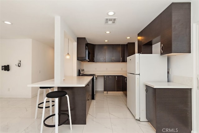 kitchen with appliances with stainless steel finishes, light marble finish floors, a peninsula, dark brown cabinets, and recessed lighting