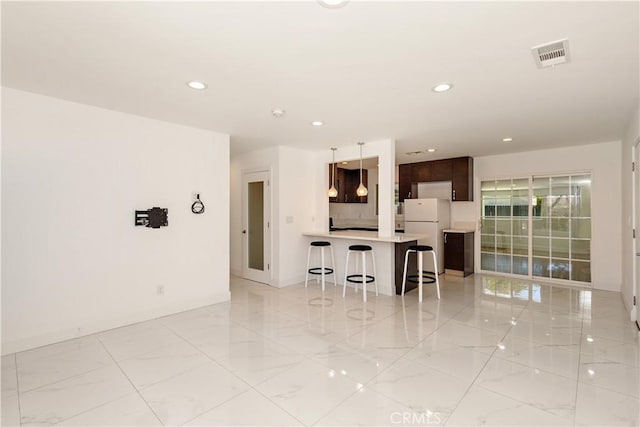 kitchen featuring freestanding refrigerator, a kitchen bar, light countertops, a peninsula, and recessed lighting