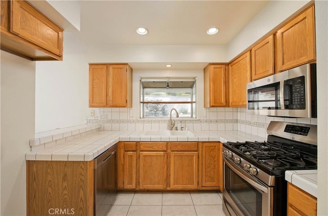 kitchen with appliances with stainless steel finishes, a sink, backsplash, light tile patterned flooring, and light countertops