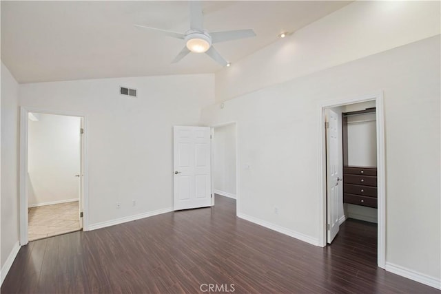 unfurnished bedroom featuring lofted ceiling, a spacious closet, dark wood-type flooring, baseboards, and a closet
