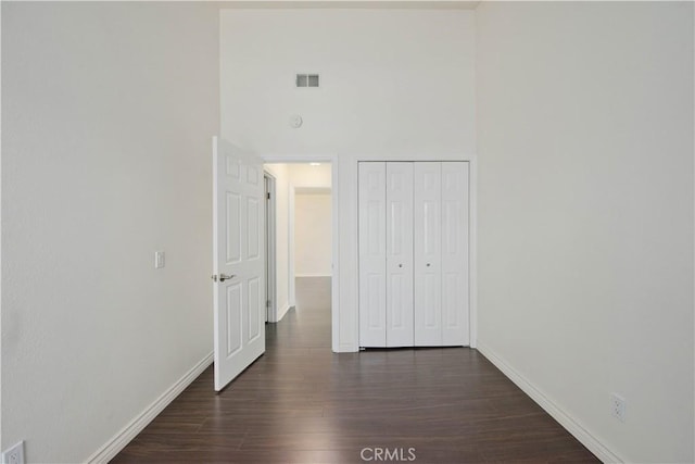 unfurnished bedroom featuring baseboards, dark wood finished floors, a towering ceiling, and a closet