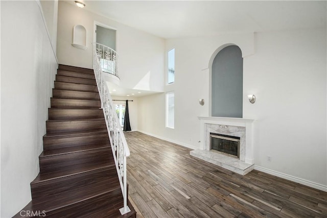 staircase with wood finished floors, a fireplace, baseboards, and a high ceiling