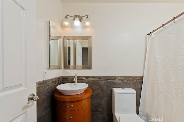 bathroom featuring tile walls, toilet, vanity, and a wainscoted wall