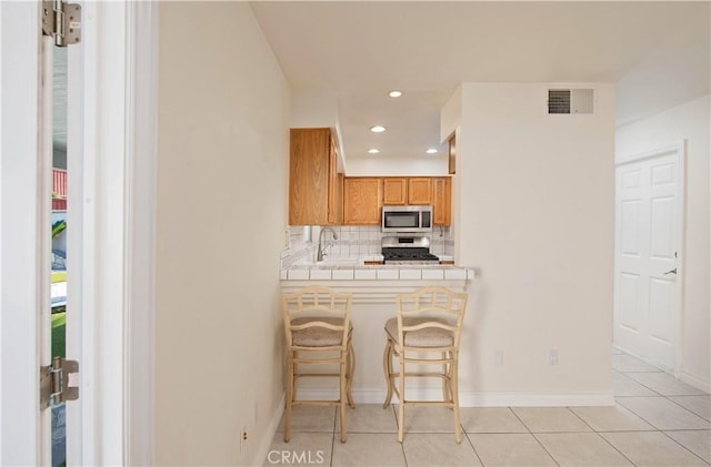 kitchen featuring stainless steel microwave, gas range, tile countertops, tasteful backsplash, and a breakfast bar