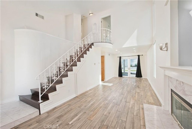 staircase featuring wood finished floors, a towering ceiling, a high end fireplace, and baseboards