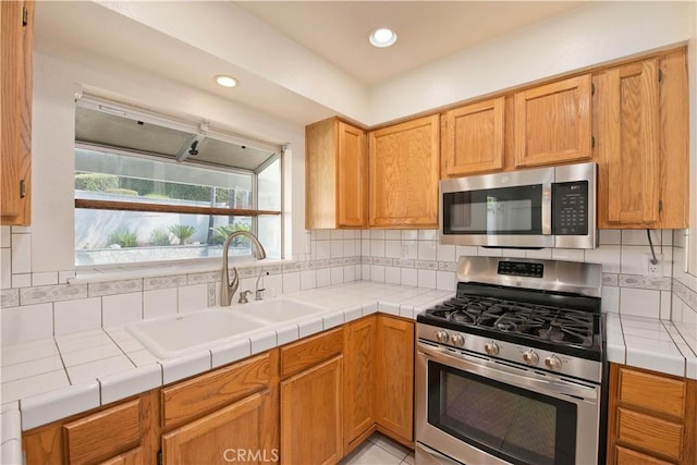 kitchen featuring appliances with stainless steel finishes, a sink, backsplash, recessed lighting, and tile countertops