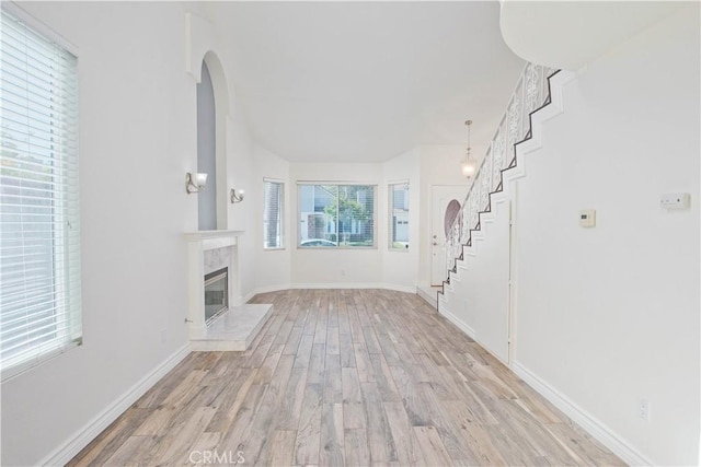 unfurnished living room with stairs, light wood-style floors, arched walkways, a high end fireplace, and baseboards