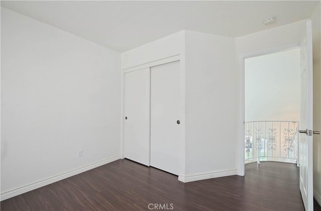 unfurnished bedroom with wood finished floors, baseboards, and a closet