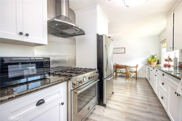 kitchen featuring stainless steel appliances, wall chimney exhaust hood, white cabinetry, and dark stone counters