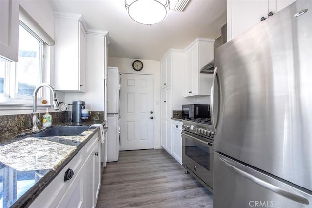 kitchen featuring appliances with stainless steel finishes, a sink, dark stone countertops, white cabinetry, and light wood-style flooring