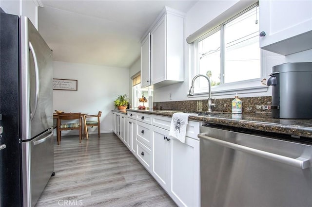 kitchen featuring stainless steel appliances, white cabinets, light wood-style flooring, and dark stone countertops