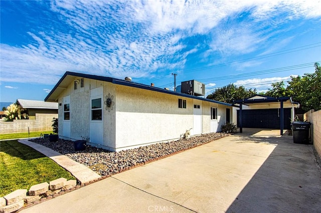 view of side of home featuring fence, central AC unit, an outbuilding, and stucco siding