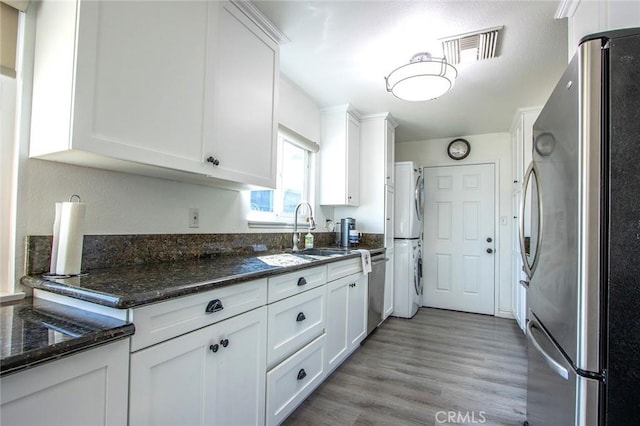 kitchen with appliances with stainless steel finishes, a sink, stacked washer / dryer, white cabinetry, and light wood finished floors