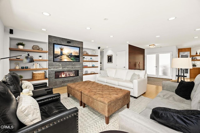 living room featuring light wood-style flooring, recessed lighting, a large fireplace, and french doors