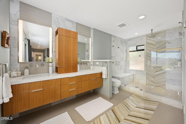 bathroom with toilet, a stall shower, tile patterned floors, double vanity, and tile walls