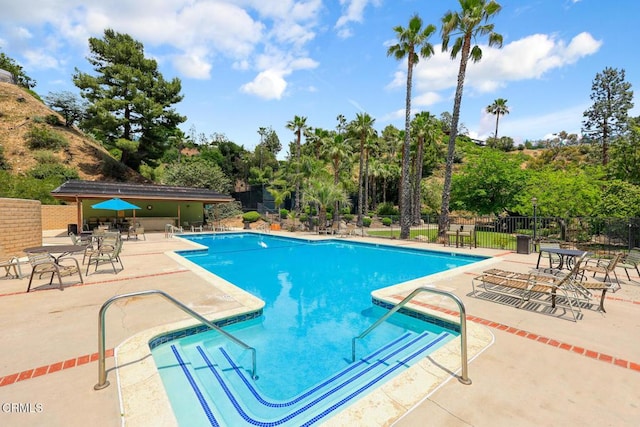 community pool with fence, a patio area, and view of scattered trees
