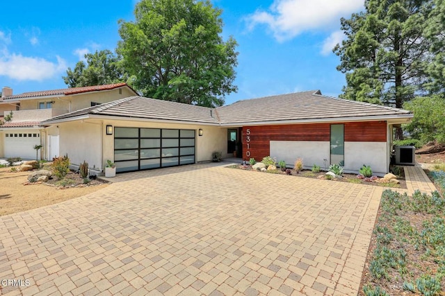 view of front facade featuring a garage, decorative driveway, a tiled roof, and stucco siding