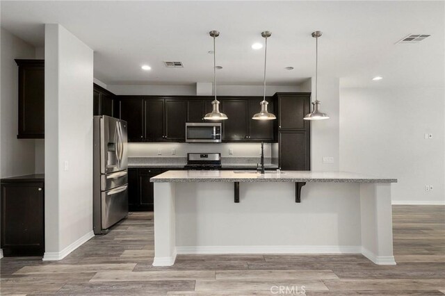 26703 Lexington Ln, Saugus, CA 91350 - kitchen featuring appliances with stainless steel finishes, a sink, a breakfast bar, light wood-style floors, and light stone countertops