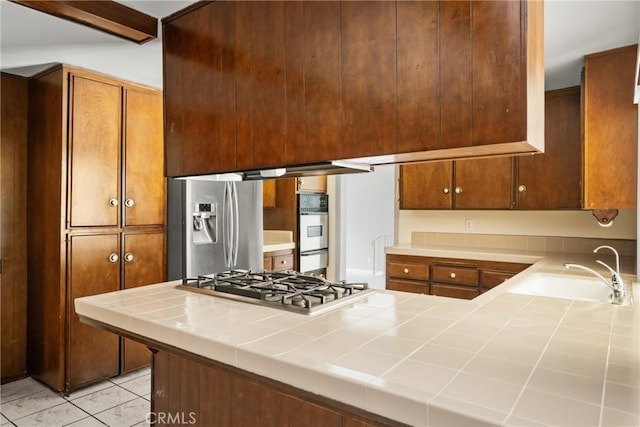 1403 W Westmont Dr, Anaheim, CA 92801 - kitchen featuring stainless steel appliances, tile countertops, a sink, a peninsula, and brown cabinets