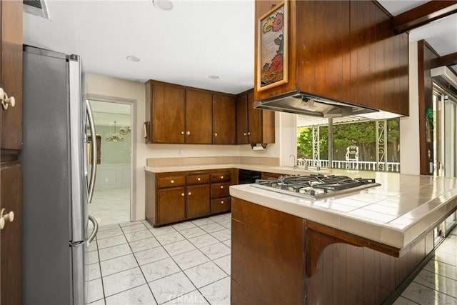 1403 W Westmont Dr, Anaheim, CA 92801 - kitchen featuring appliances with stainless steel finishes, tile countertops, light marble finish floors, under cabinet range hood, and brown cabinetry