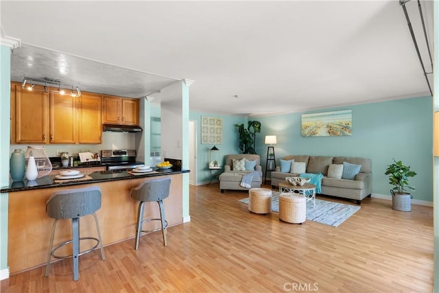 810 Camino Real Unit 104, Redondo Beach, CA 90277 - kitchen featuring stainless steel range with electric stovetop, under cabinet range hood, dark countertops, light wood finished floors, and a kitchen breakfast bar