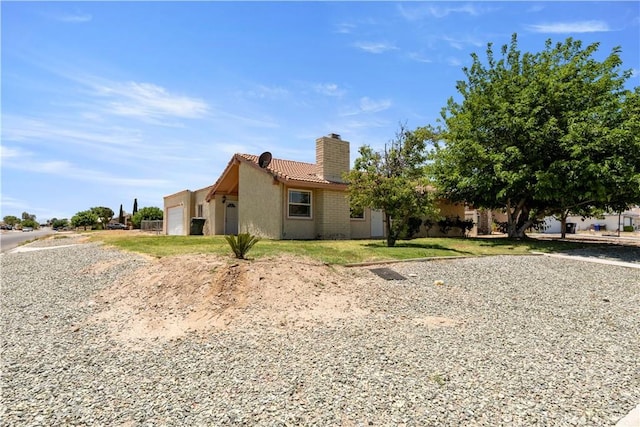 14889 Hartford Ln, Helendale, CA 92342 - view of home's exterior with a chimney, a tiled roof, an attached garage, stucco siding, and driveway