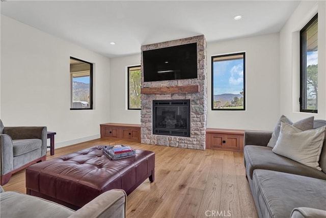 living room with light wood-style floors, a stone fireplace, recessed lighting, and baseboards