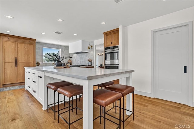 kitchen with stainless steel double oven, a kitchen breakfast bar, light wood-type flooring, a spacious island, and light stone countertops
