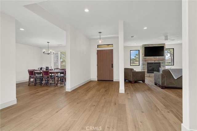 entrance foyer with light wood-style floors, a fireplace, a chandelier, baseboards, and a ceiling fan