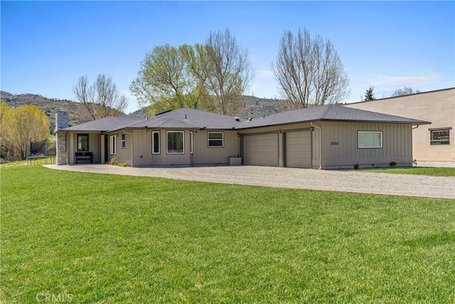 back of house with an attached garage, a chimney, gravel driveway, a lawn, and board and batten siding