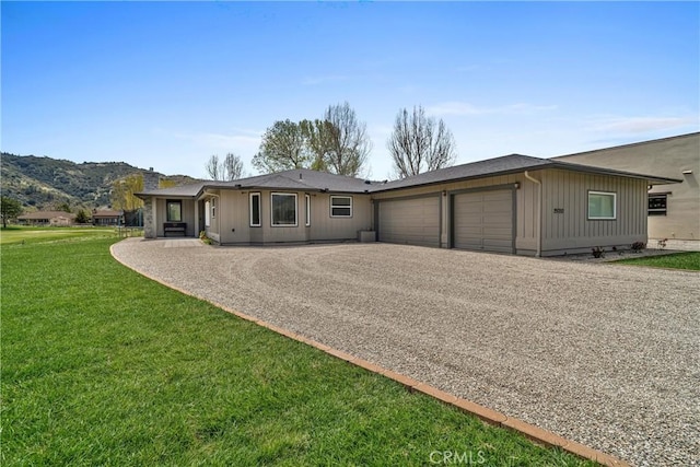view of front facade featuring a garage, driveway, a front yard, board and batten siding, and a mountain view