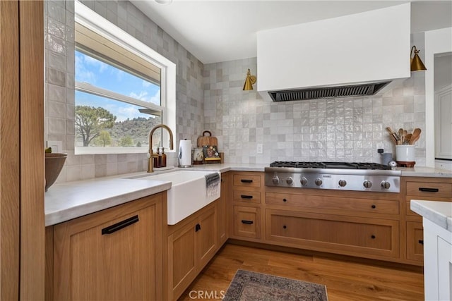 kitchen with a sink, custom exhaust hood, stainless steel gas stovetop, light countertops, and tasteful backsplash