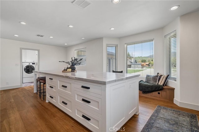 kitchen featuring washer / dryer, light stone countertops, wood finished floors, a center island, and recessed lighting