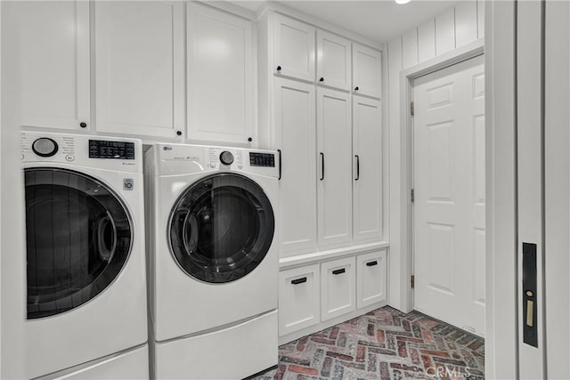clothes washing area with washing machine and clothes dryer, cabinet space, and brick patterned flooring