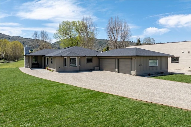 back of house featuring a garage, driveway, a lawn, a mountain view, and a chimney