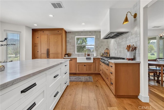 kitchen featuring a sink, stainless steel gas cooktop, decorative backsplash, custom range hood, and plenty of natural light
