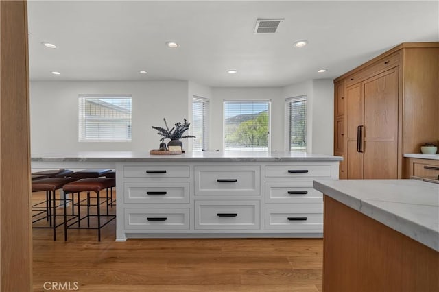 kitchen with light stone countertops, white cabinets, recessed lighting, a kitchen bar, and light wood-style flooring