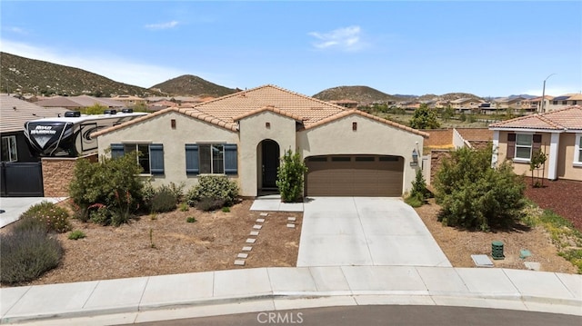 mediterranean / spanish house featuring a garage, stucco siding, concrete driveway, a tile roof, and a mountain view