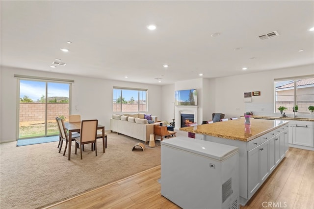 27083 Comrade Cir, Menifee, CA 92585 - kitchen with fridge, recessed lighting, a kitchen island, light wood finished floors, and a glass covered fireplace