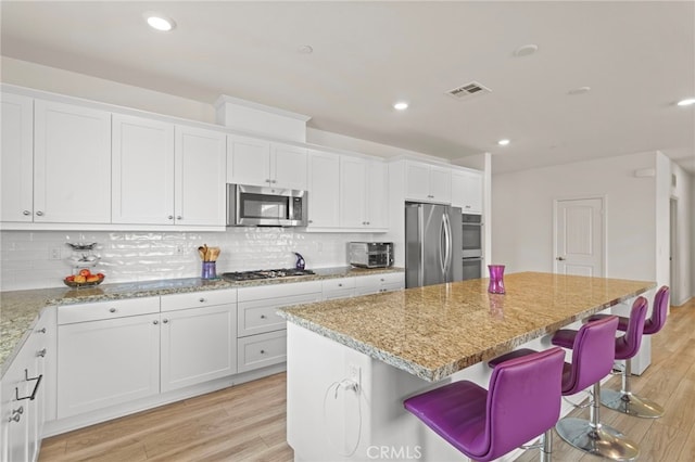 27083 Comrade Cir, Menifee, CA 92585 - kitchen featuring appliances with stainless steel finishes, a center island, white cabinets, a kitchen bar, and light stone counters