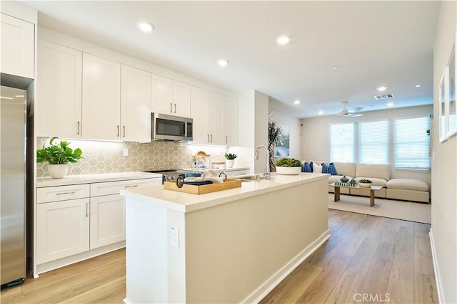 kitchen with stainless steel appliances, a sink, white cabinets, light wood-type flooring, and recessed lighting