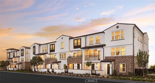 townhome / multi-family property featuring stucco siding, a tiled roof, and brick siding