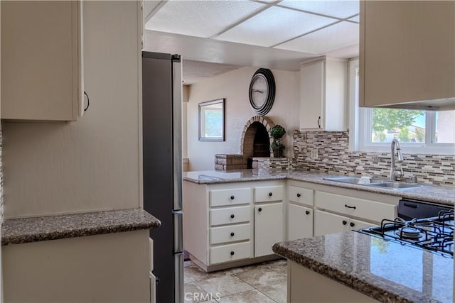 kitchen with a sink, freestanding refrigerator, tasteful backsplash, and white cabinets